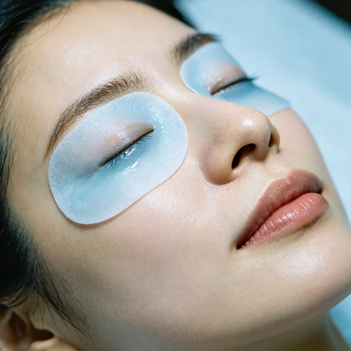 person applying a cool compress to their eyes after a treatment