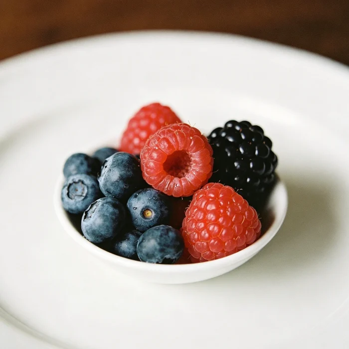 A small bowl of mixed blueberries, raspberries, and blackberries on a white plate